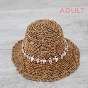 Puede incluir: Un sombrero de sol de crochet marr&oacute;n con una banda de flores rosas, blancas y azules.