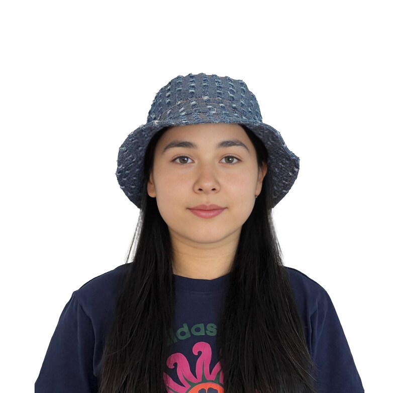 K&ouml;nnte beinhalten: Eine Person tr&auml;gt einen blauen Jeans-Bucket-Hut mit wei&szlig;em Muster. Der Hut hat eine breite Krempe und eine leicht abgerundete Krone. Die Person tr&auml;gt ein dunkelblaues Shirt mit einem bunten Grafikdesign.