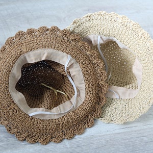 Puede incluir: Dos sombreros de paja con ribete de ganchillo. Un sombrero es marr&oacute;n y el otro es beige.