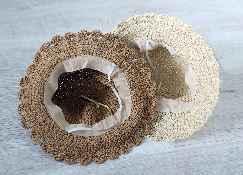 Puede incluir: Dos sombreros de paja con ribete de ganchillo. Un sombrero es marr&oacute;n y el otro es beige.