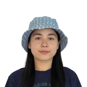K&ouml;nnte beinhalten: Eine Person tr&auml;gt einen blauen Jeans-Bucket-Hut mit wei&szlig;em Muster. Der Hut hat einen ausgefransten Rand.