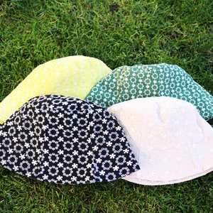May include: Four bucket hats in different colors and patterns. The hats are made of a soft, textured fabric and have a wide brim. The hats are arranged in a circle on a bed of green grass.