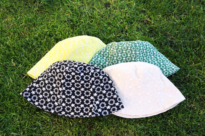 May include: Four bucket hats in different colors and patterns. The hats are made of a soft, textured fabric and have a wide brim. The hats are arranged in a circle on a bed of green grass.