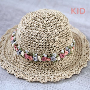 Puede incluir: Un sombrero de paja para el sol con un borde de crochet y una banda de flores de tela rosa, blanca y gris.