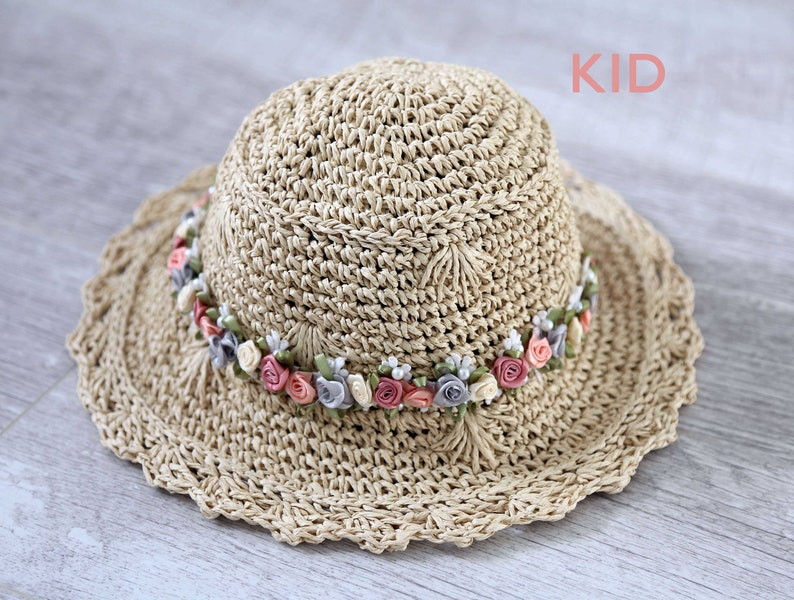 Puede incluir: Un sombrero de paja para el sol con un borde de crochet y una banda de flores de tela rosa, blanca y gris.