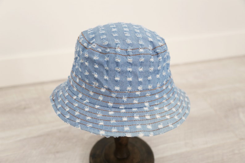 K&ouml;nnte beinhalten: Ein hellblauer Jeans-Bucket-Hut mit Used-Look. Der Hut hat eine breite Krempe und ein gen&auml;htes Design.