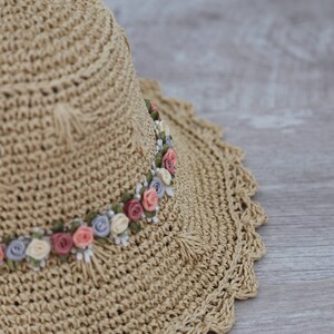 Puede incluir: Un sombrero de paja con un borde de crochet y una banda de flores de tela en tonos de rosa, blanco y azul.