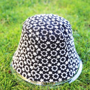 May include: A black bucket hat with a white floral pattern. The hat is sitting on a green grassy surface.