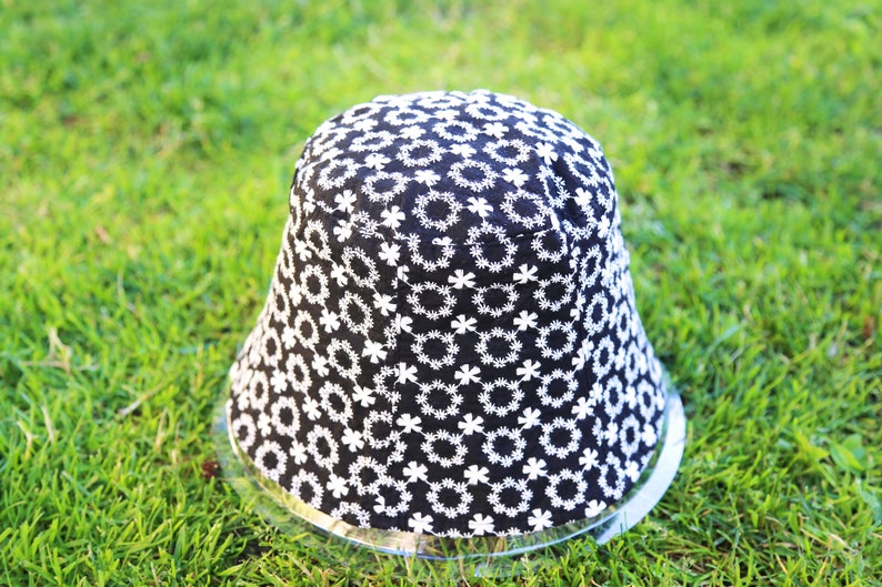May include: A black bucket hat with a white floral pattern. The hat is sitting on a green grassy surface.