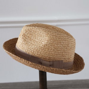 May include: A light brown straw fedora hat with a brown ribbon band.