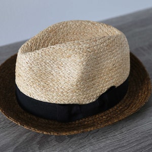 May include: A brown and tan straw hat with a black ribbon around the crown.