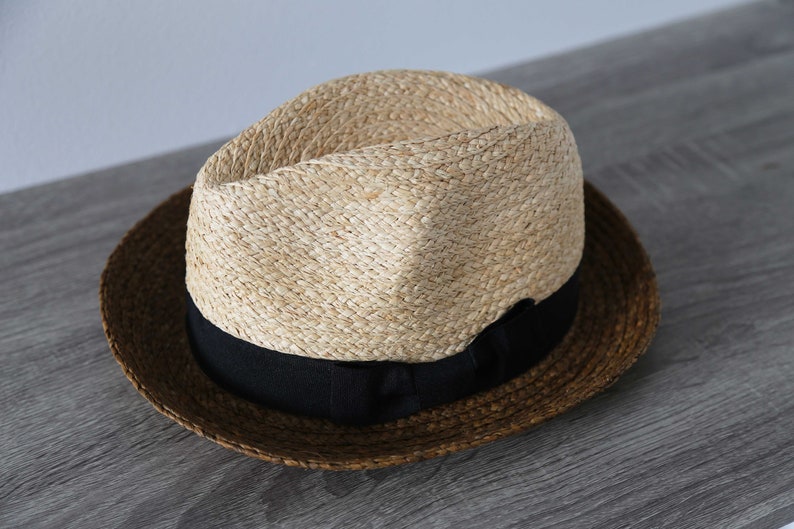 May include: A brown and tan straw hat with a black ribbon around the crown.
