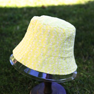 May include: A yellow bucket hat with a white floral pattern. The hat is made of a soft, lightweight fabric and has a wide brim.