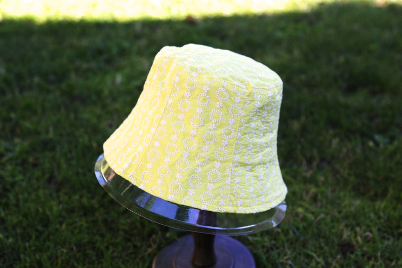 May include: A yellow bucket hat with a white floral pattern. The hat is made of a soft, lightweight fabric and has a wide brim.