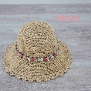 Puede incluir: Un sombrero de sol de crochet beige con un borde festoneado y una banda de flores rosas, blancas y moradas.