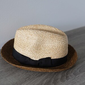 May include: A brown and tan straw hat with a black ribbon around the crown.