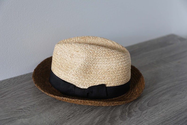May include: A brown and tan straw hat with a black ribbon around the crown.