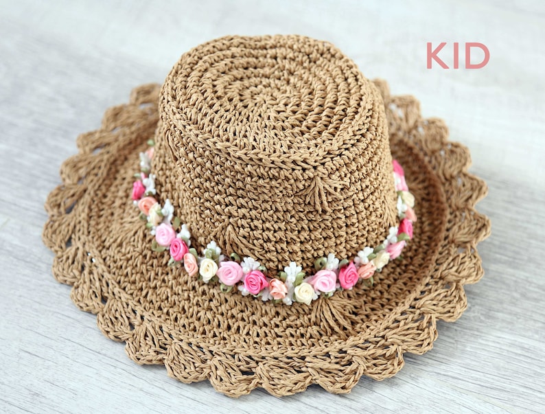 Puede incluir: Un sombrero de paja marr&oacute;n con un borde de ganchillo y una banda de flores rosas y blancas.