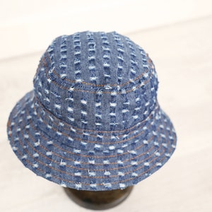 K&ouml;nnte beinhalten: Ein blauer Jeans-Bucket-Hut mit Used-Look. Der Hut hat eine breite Krempe und ein gen&auml;htes Design.