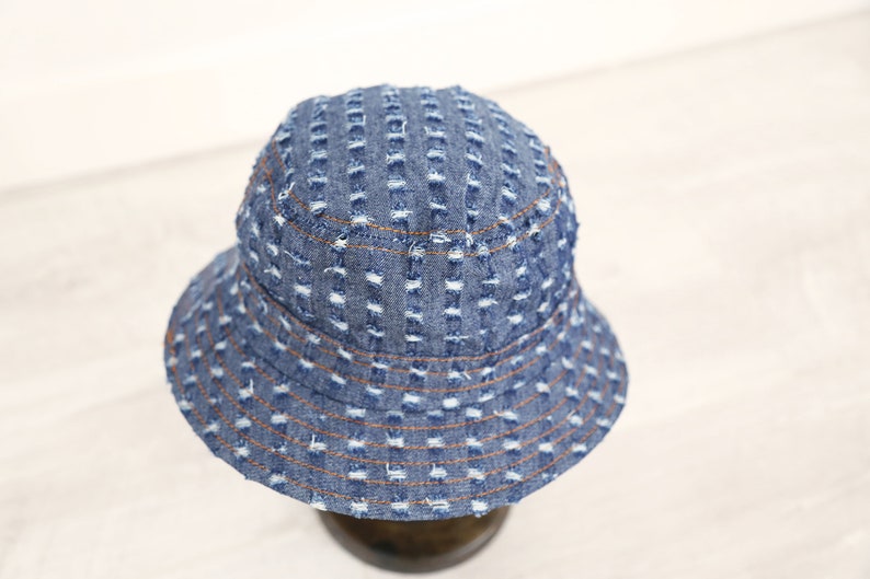 K&ouml;nnte beinhalten: Ein blauer Jeans-Bucket-Hut mit Used-Look. Der Hut hat eine breite Krempe und ein gen&auml;htes Design.