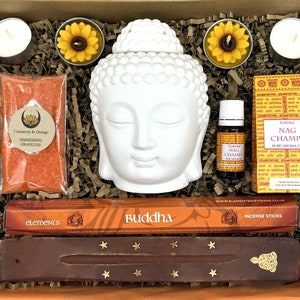 May include: A gift box filled with items for relaxation and meditation. The box includes a white Buddha head incense burner, a pack of incense sticks, a bottle of essential oil, a pack of simmering granules, and two tea lights.