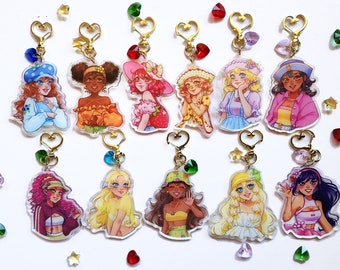 May include: Twelve colorful acrylic keychains featuring cartoon characters with different hairstyles, outfits, and accessories. Each keychain has a gold heart-shaped ring and a small crystal charm.