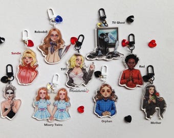 May include: A set of 10 zipper pulls featuring horror movie characters. The characters include: Black Swan, Misery Twins, Orphan, Mother, Red, TV Ghost, Robodoll, Sandie, Tiff, and a character with the text "Manicheric" on the pull.