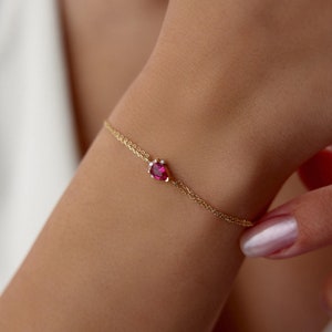 May include: A delicate gold chain bracelet with a single pear-shaped ruby gemstone surrounded by smaller diamonds.
