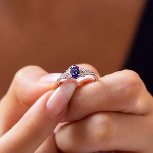 Könnte beinhalten: Ein silberner Ring mit einem blauen ovalen Edelstein und kleinen klaren Edelsteinen auf der Ringschiene.
