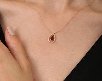 Op de afbeelding: Een gouden ketting met een traanvormige hanger met een rode edelsteen.