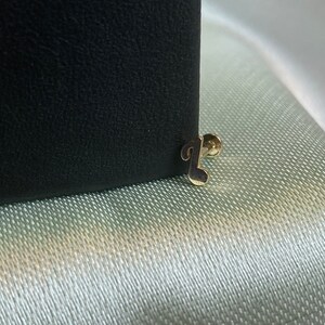 May include: A gold musical note stud earring. The earring is on a black background.