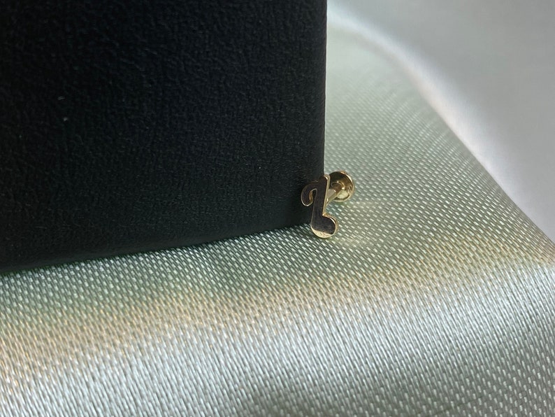 May include: A gold musical note stud earring. The earring is on a black background.