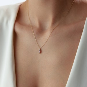 Peut inclure: Un collier en chaîne dorée avec un petit pendentif orné d'une pierre rouge entourée de petites pierres blanches.