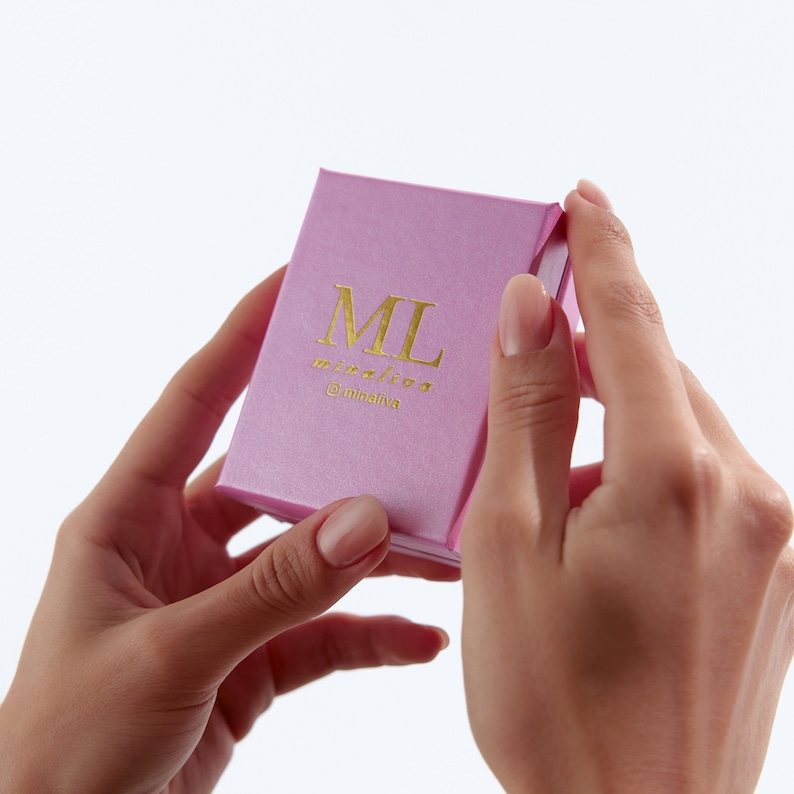 May include: A pink box with the letters "ML" in gold lettering and the text "minilive @minilive" in gold lettering.