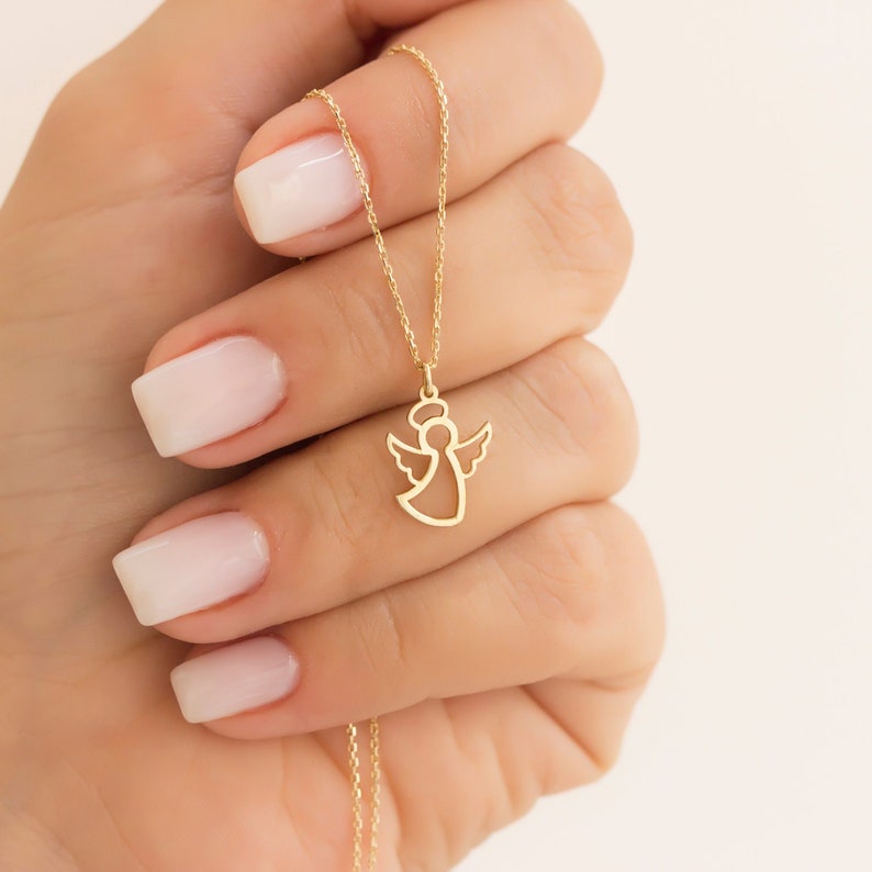 May include: A gold chain necklace with a delicate angel pendant. The angel is outlined in gold and has wings.