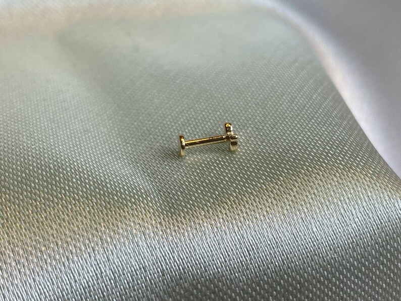 May include: A gold nose ring with a small, clear gemstone.