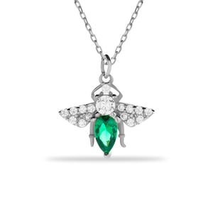 Puede incluir: Un collar de plata con un colgante de abeja con una piedra de esmeralda verde y piedras de circonita c&uacute;bica transparentes.