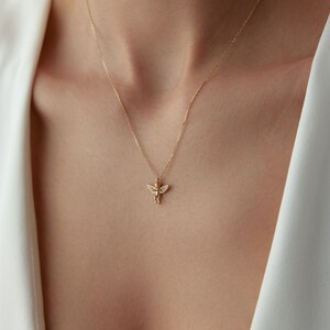 May include: A gold chain necklace with a small angel pendant featuring clear cubic zirconia stones.