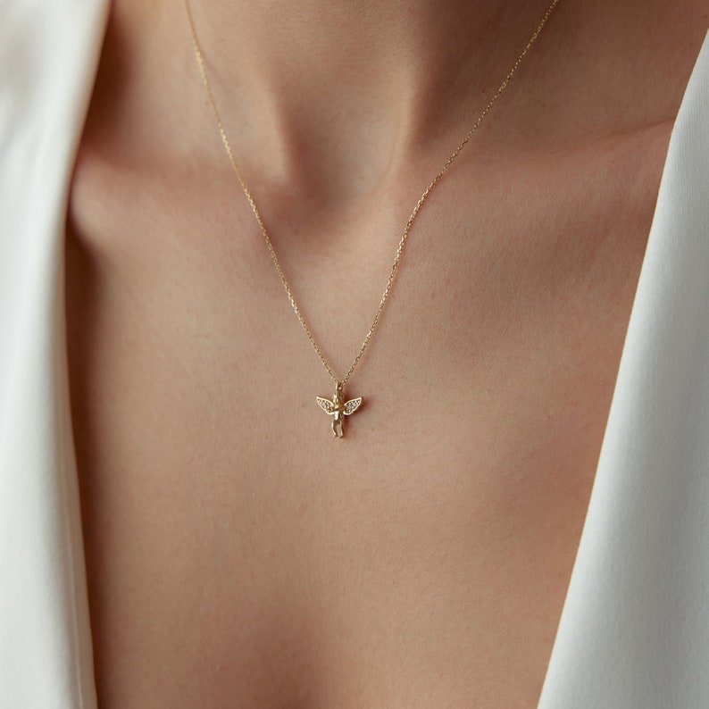 May include: A gold chain necklace with a small angel pendant featuring clear cubic zirconia stones.