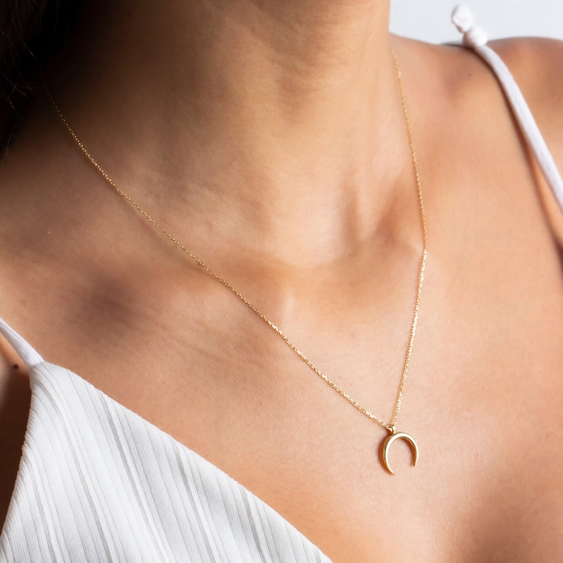 Puede incluir: Un collar de cadena de oro con un colgante de media luna.