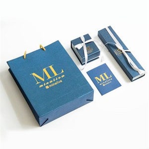 Puede incluir: Una bolsa de regalo azul con el texto "ML" y "minimalive" en letras doradas. La bolsa est&aacute; junto a una peque&ntilde;a caja de regalo azul con una cinta blanca y una caja azul m&aacute;s grande con una cinta blanca. Tambi&eacute;n hay una peque&ntilde;a tarjeta azul con el texto "ML" y "minimalive" en letras doradas.
