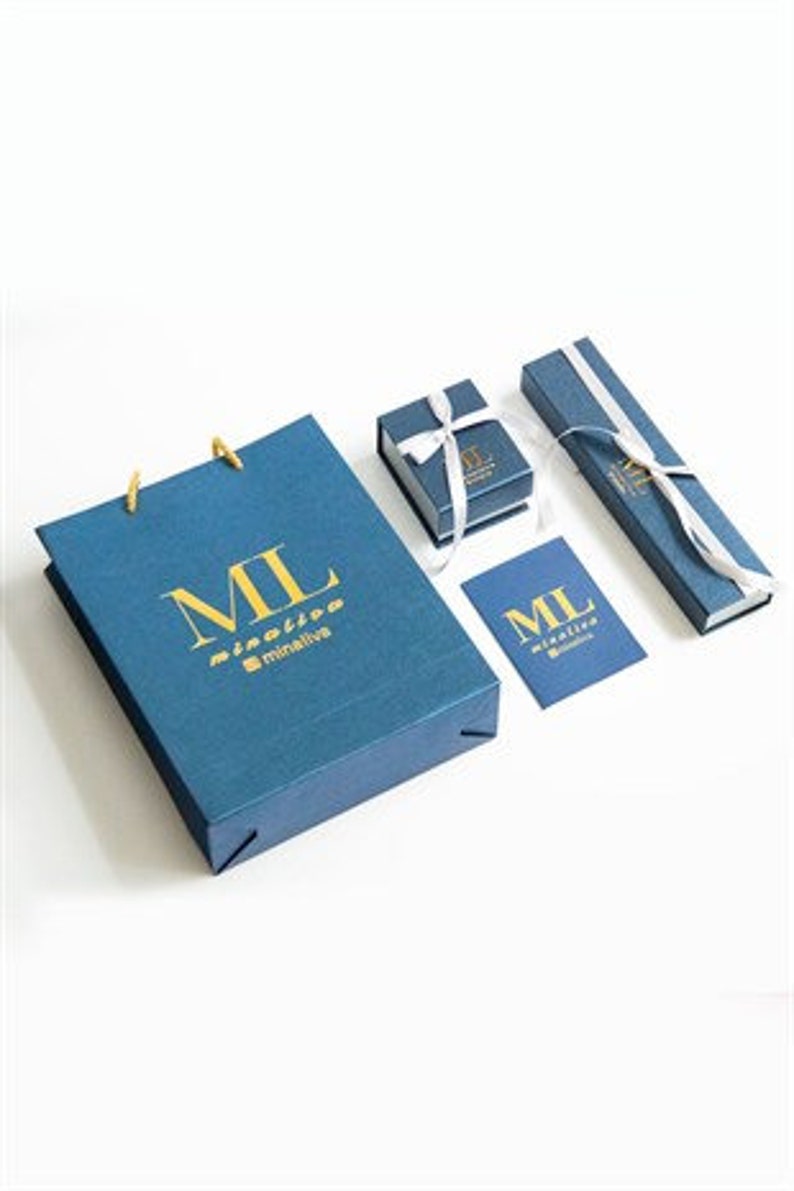 Puede incluir: Una bolsa de regalo azul con el texto "ML" y "minimalive" en letras doradas. La bolsa est&aacute; junto a una peque&ntilde;a caja de regalo azul con una cinta blanca y una caja azul m&aacute;s grande con una cinta blanca. Tambi&eacute;n hay una peque&ntilde;a tarjeta azul con el texto "ML" y "minimalive" en letras doradas.