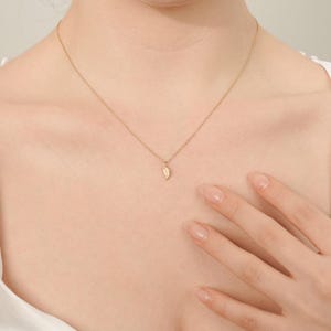 May include: A delicate gold necklace with a small, leaf-shaped pendant. The pendant is set with tiny, sparkling stones.