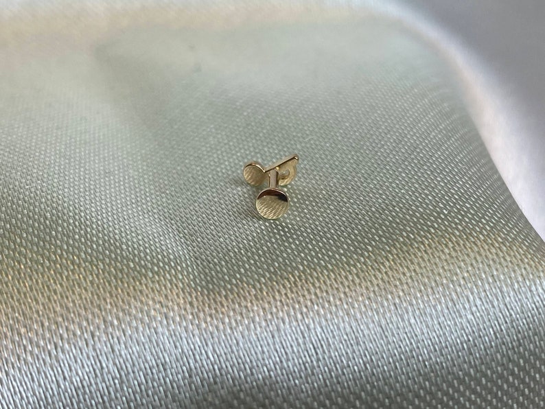 May include: A gold-colored stud earring with a round top and a post.