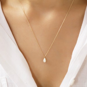 Minimalist Drop Shaped 14K Necklace Rests On The Model’s neck. It is a Handmade Pendant With a Dainty, White Colored Opal Stone On The Chain