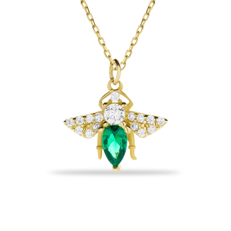 Puede incluir: Un collar con un colgante de abeja de oro, adornado con una esmeralda verde y piedras de circonita c&uacute;bica transparentes.