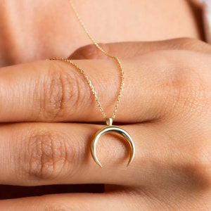 Puede incluir: Un collar de cadena de oro con un colgante de media luna.