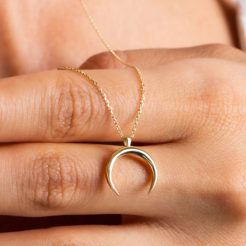 Puede incluir: Un collar de cadena de oro con un colgante de media luna.