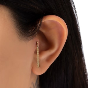 Puede incluir: Un pendiente de cadena dorada con pequeñas cuentas que cuelgan del lóbulo de la oreja.