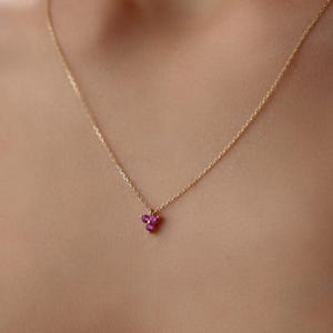 May include: A delicate gold chain necklace with a small pendant featuring three tiny ruby red gemstones.